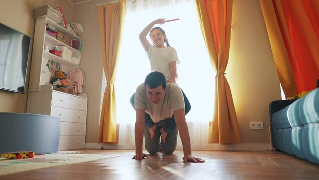 dad playing with baby at home. happy family kid dream concept. dad plays with his daughter rolls her on his back kneels on the floor fun funny. baby and dad play at home lifestyle