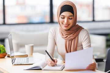 beautiful smiling muslim woman in traditional religious hijab works remotely on laptop from home
