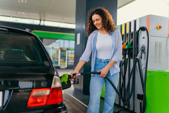 A beautiful woman with curly hair is filling her car tank while taking a break on her road trip