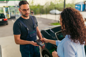 Fototapeta premium A young woman pays for fuel at a gas station using a card, the worker gave her a terminal to pay