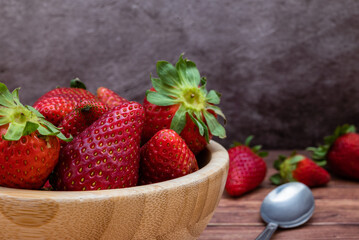 Sweet red strawberries in a wooden bowl placed on a table. Teaspoon and selective focus.