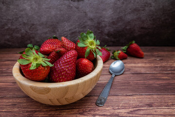 Sweet red strawberries in a wooden bowl placed on a table. Teaspoon and selective focus.