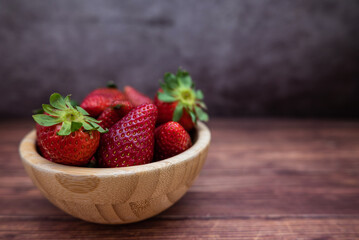 Sweet red strawberries in a wooden bowl placed on a table. Selective focus.