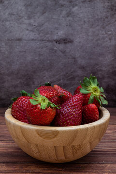 Sweet red strawberries in a wooden bowl placed on a table. Vertical image with selective focus.