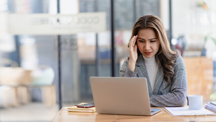 Stressed and frustrated asian female accountant sitting at desk making serious business decisions Worried about the project she's working on and the pain in her eyes looking at the screen?