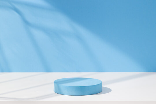 Cylinder podium for products or cosmetics against light blue background with window shadow.	