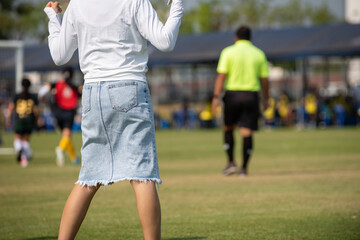 Mother standing and watching her son playing football in a school tournament on a clear sky and...