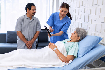 Nurse showing medical insurance data in digital tablet near bed of patient with relative stand by