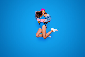 Obraz premium Full length size studio photo shooting portrait of cheerful joyful careless fresh cool with toothy beaming smile girl jumping up with skate board in hand isolated bright pastel background