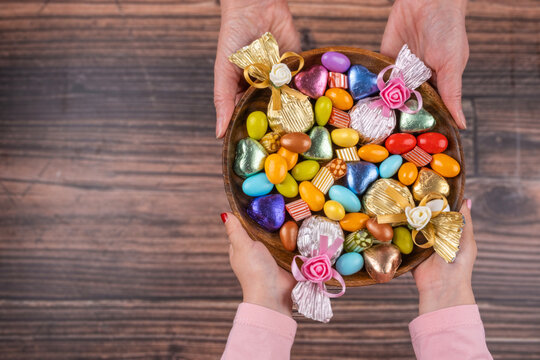 Chocolate candies, top view image of woman and child hand holding bowl of chocolate candies. Wooden background, copy space. Traditional Turkish feast called Ramazan Bayram. Almond dragee sweets.