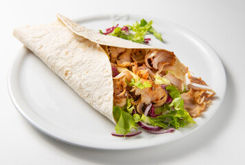 Rolled piadina with rich filling of kebabs, vegetables, onion and sauces, horizontal food photography with subject in center isolated on white plate and neutral white table, natural light