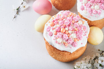 Traditional Easter sweet bread or cakes with white icing and sugar decor, colored eggs and cherry blossom tree branch over white table. Various Spring Easter cakes. Happy Easter day. Selective focus.