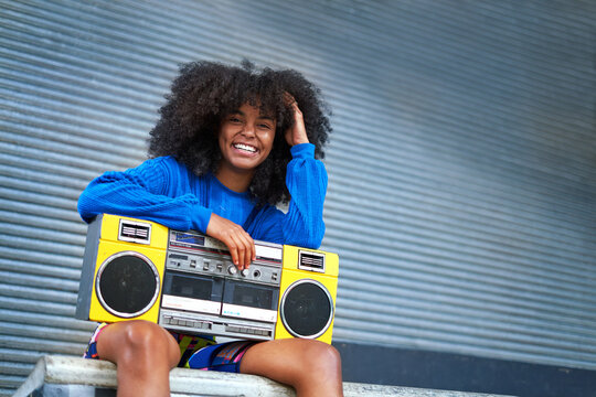 Portrait happy, cool young woman with boom box in alley