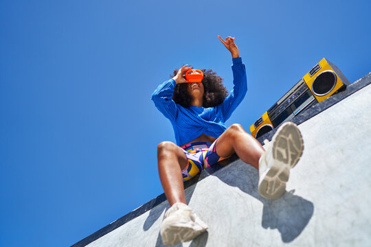 Young woman with boom box using view finder against blue sky