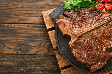 Steaks T-bone. Sliced beef grilled T-bone or porterhouse meat steak with spices rosemary and pepper on black marble board on old wooden background. Top view. Mock up.