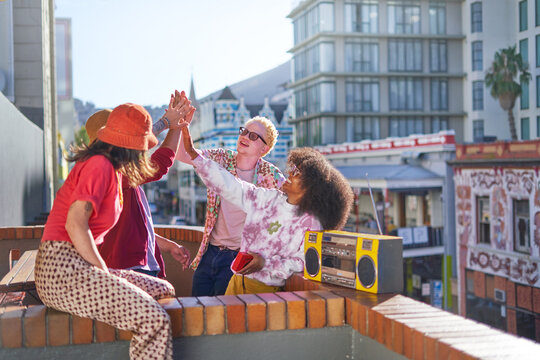 Happy young friends high-fiving on sunny urban city balcony