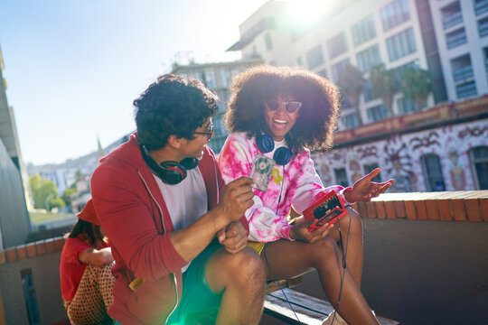 Happy young friends listening to music on sunny urban balcony