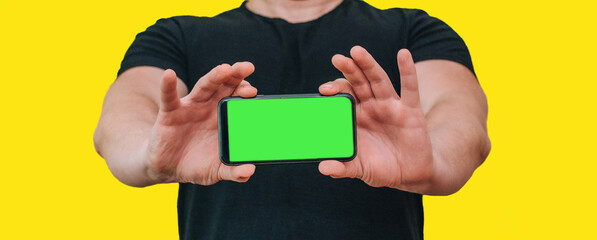 Close-up of a man holding a new black smartphone with a blank screen. Mobile phone with green screen copy text
