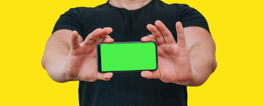 Close-up of a man holding a new black smartphone with a blank screen. Mobile phone with green screen copy text