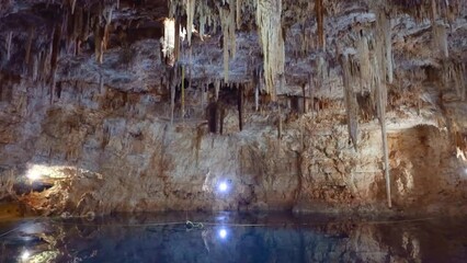 Cenote, Yucatan, Mexico, panning shot of subterranean pool with crystal blue waters and light reflections on the roof with stalactites