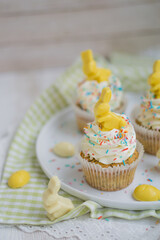 Lemon poppy seeds cupcakes with white whipped buttercream and white and yellow chocolate bunnies and coloreful sprinkles easter baking close up selective focus