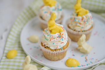Lemon poppy seeds cupcakes with white whipped buttercream and white and yellow chocolate bunnies and coloreful sprinkles easter baking close up selective focus