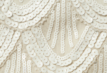 Wavy sequins pattern on white decorative fabric background. Abstract embroidery of small round sequins on clothing material close-up