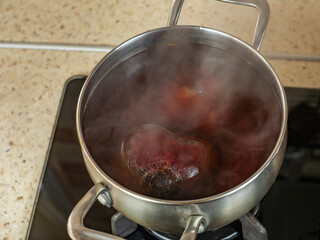 Gas home stove with red beets boiled on it in a stainless steel saucepan with a transparent glass...