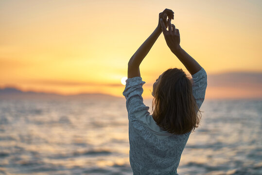 Back View Carefree Woman With Hands Up To The Sky At Sunset Over The Sea. Silhouette Of Dreamer Girl Looking Hopeful At The Horizon