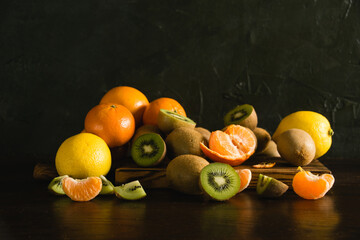 Sweet fruits on a dark background. Tangerines, lemons, kiwis, whole fruits and pieces on a wooden cutting board
