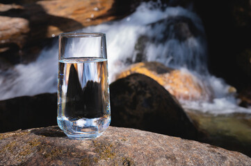 Clean water, healthy concept. Natural drinking water in a glass glass stands on a stone against the backdrop of a river, nature