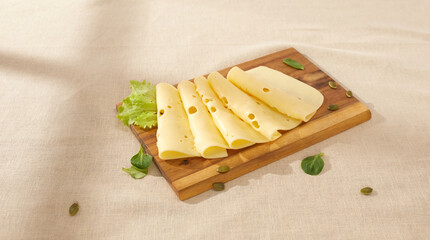 slices of cheese with herbs on a wooden board. maasdam on a light background. yellow cheese under sunlight. dairy products on the table