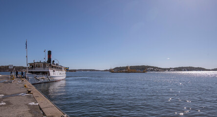 Old steam ship at the jetty in the archipelago town Vaxholm, an Trafikverkets yellow road ferry in background passing. a sunny spring day in Stockholm