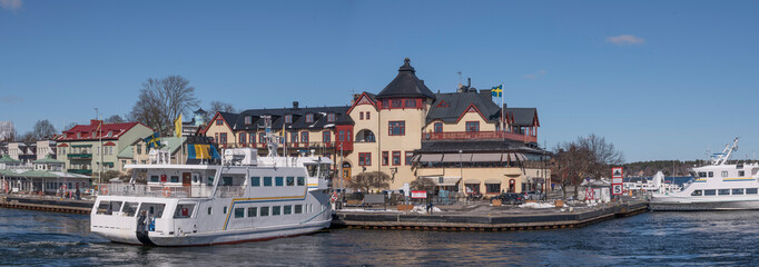 Fototapeta premium Commuter archipelago ferries in the bay at the archipelago town Vaxholm, famous fortress and hotel, a sunny spring day in Stockholm