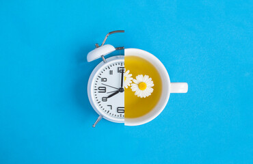 Collage of alarm clock and tea with chamomile flower in the white cup on the blue background. Top...