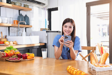 A young woman with a beautiful face in a blue shirt with long hair eating fruit sitting inside the kitchen at home with a laptop and notebook for relaxation, Concept Vacation.