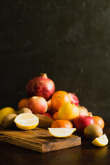 Fruit in a reusable bag. Earth day and zero waste concept. Sliced lemon on cutting board, pomegranate, orange, tangerine, apple and kiwi on dark background