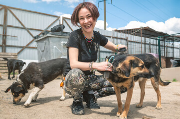 Dog at the shelter. Animal shelter volunteer feeding the dogs. Dogs in cage with cheerful woman...