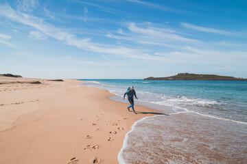 Young, passionate black-haired dobby runs from the waves of the Atlantic Ocean on a sandy beach near Porto Covo, Portugal. In the footsteps of Rota Vicentina