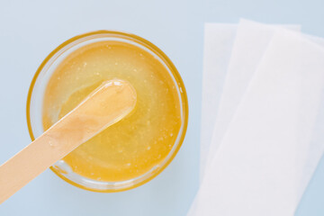 Liquid yellow sugar paste, wooden spatula, depilatory strips on a blue background. Removing unwanted hair. Sugaring. Depilation. Epilation. Beauty. Top view.