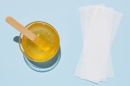 Liquid yellow sugar paste, wooden spatula, depilatory strips on a blue background. Removing unwanted hair. Sugaring. Depilation. Epilation. Beauty. Top view.