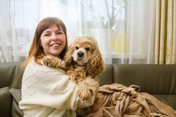 A young woman is holding a Cocker Spaniel in her arms while sitting on the sofa.