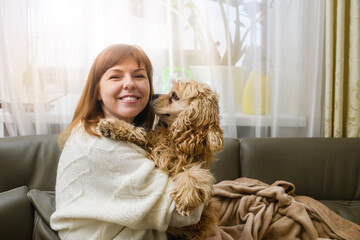 A young woman is holding a Cocker Spaniel in her arms while sitting on the sofa.