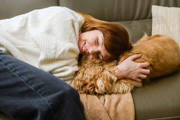 Cute young caucasian woman hostess caresses american cocker spaniel, pressing her face against him.