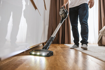 Cropped picture of a man using modern vacuum cleaner to clan up under the furniture.
