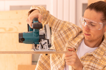 Craftsman with circular saw fixing furniture. Male woodworker in safety goggles cutting wooden construction with circular saw on workbench