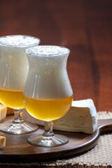 Glasses of Belgian light blonde beer made in abbey and wooden board with variety of belgian cheeses