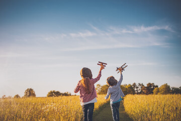 Boy and girl plaing with wooden planes on the field in sunset