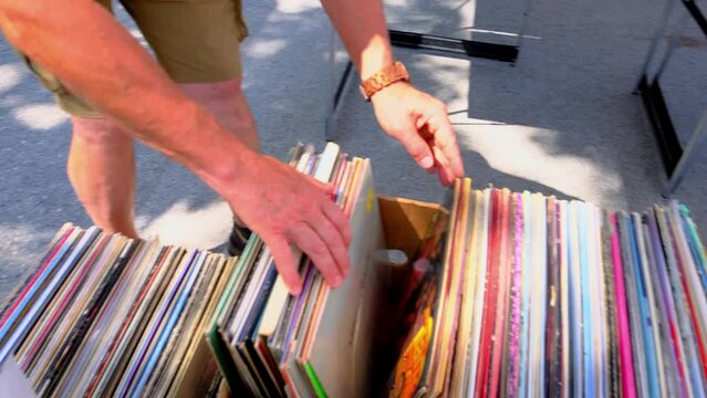 flea market flip in the city, man choosing vinyl records, antiques, old furniture, tables, used things, clothes and other goods are sold on street, recycling of unwanted items, pollution of nature