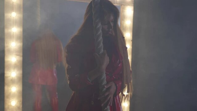 sexy red haired woman in red leather with moving seductively in room with big mirror